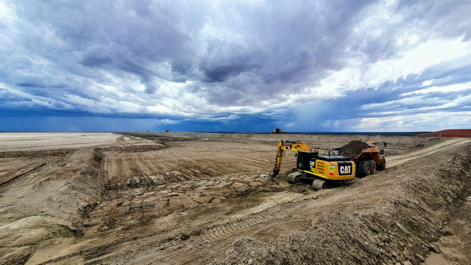 Large scale earthworks with excavator and dump truck under storm clouds
