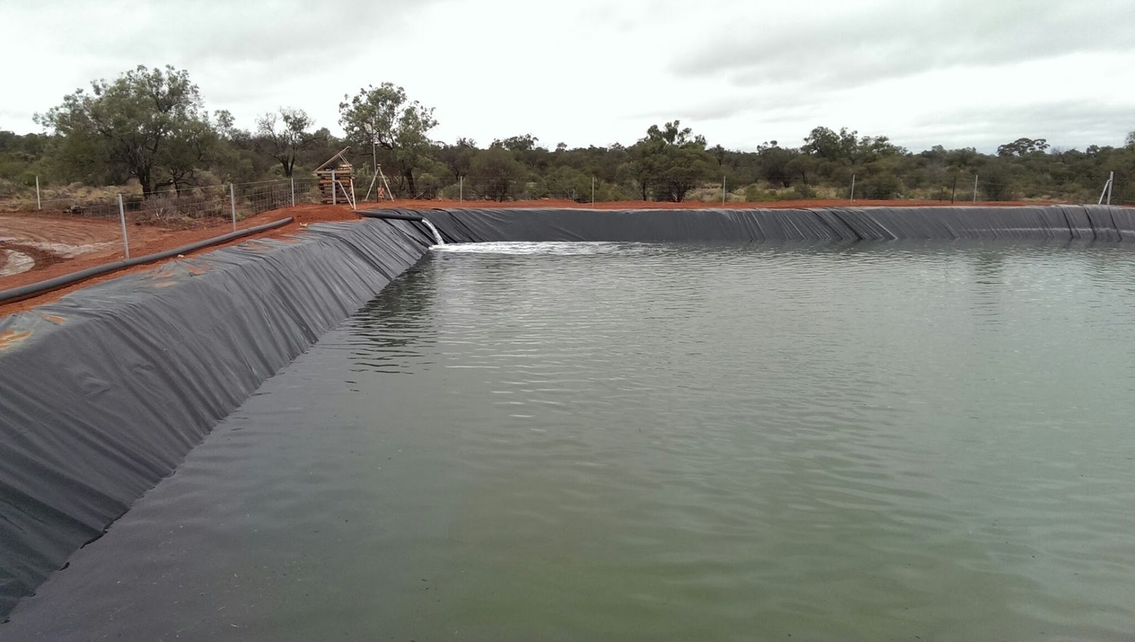 Lined water containment pond under overcast skies